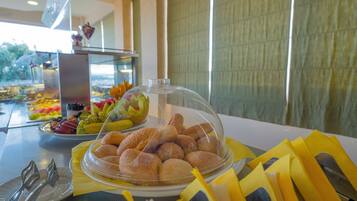 Une table de buffet proposant une variété de plats, notamment du pain et des fruits, le tout recouvert d’un couvercle en verre.