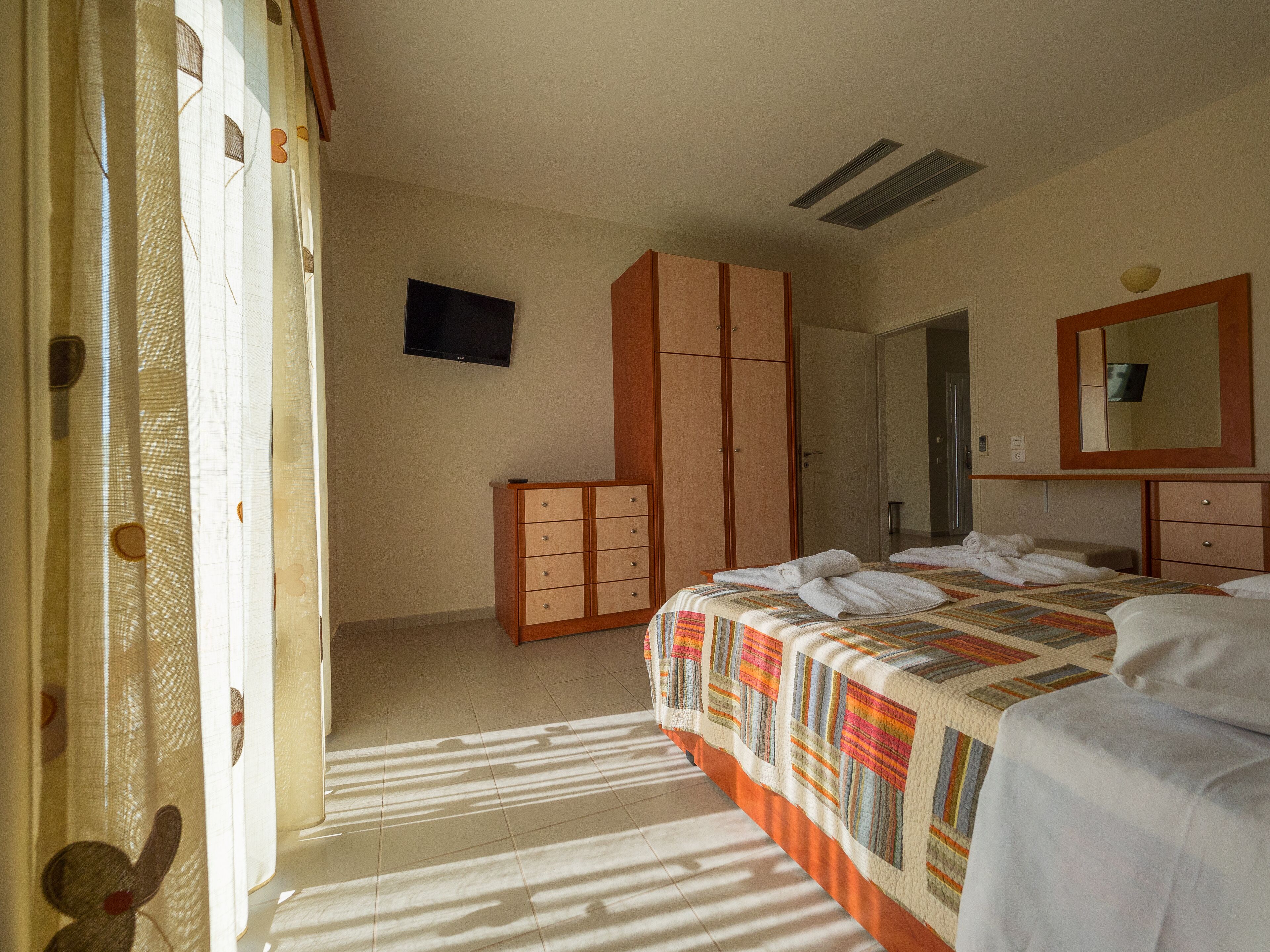 A hotel room with a bed, a wardrobe, a television, and a mirror.