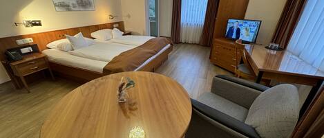 Een hotelkamer met een bed, een houten tafel, een bank, een televisie en een aan de muur bevestigd telefoontoestel.