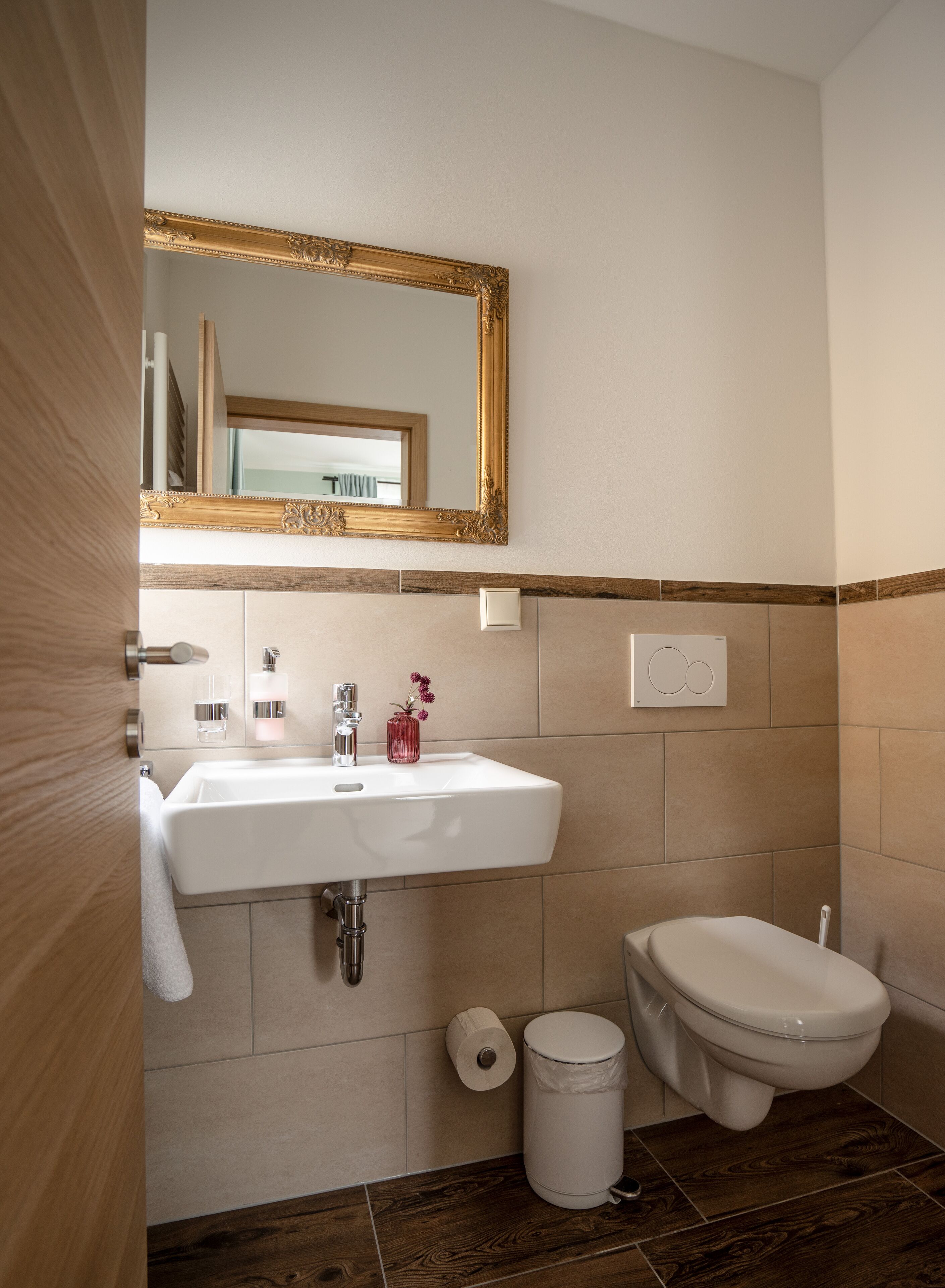 Un baño moderno con un lavamanos blanco, un inodoro y un espejo con un marco decorado.