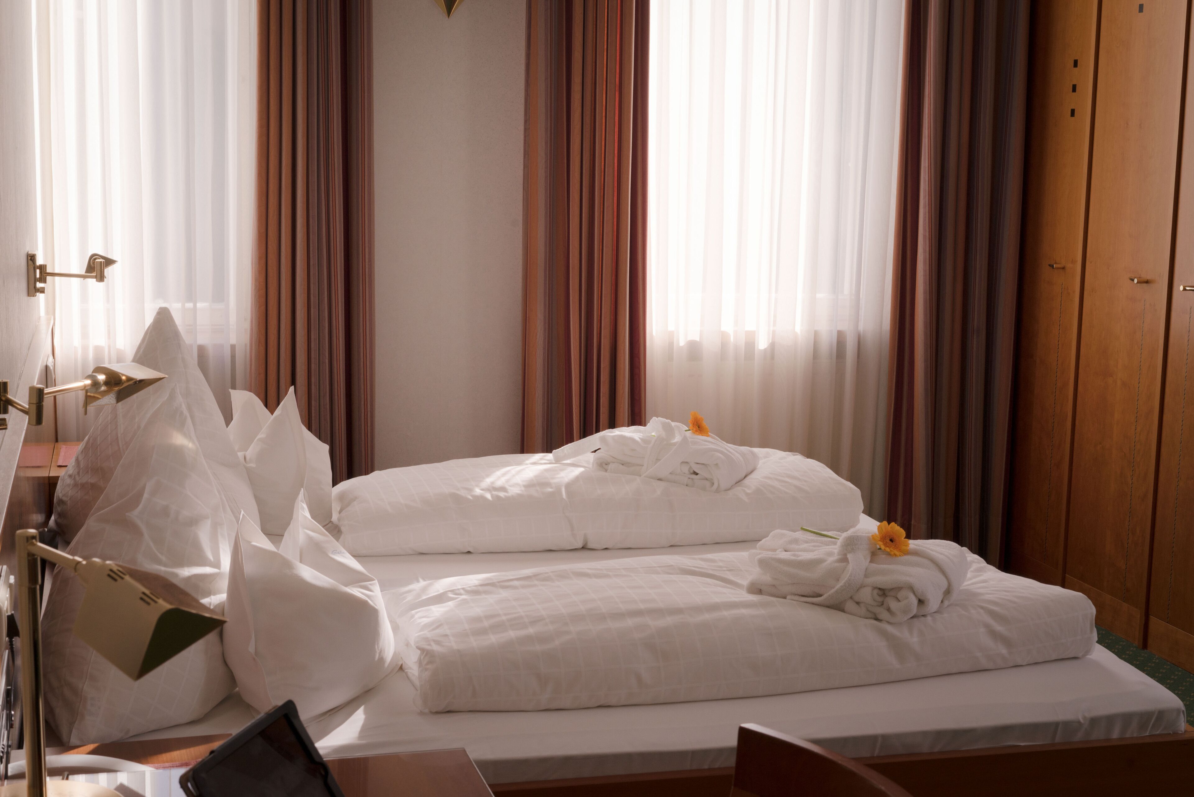 Camera d'albergo con due letti, un comodino, una lampada e una finestra con tende.