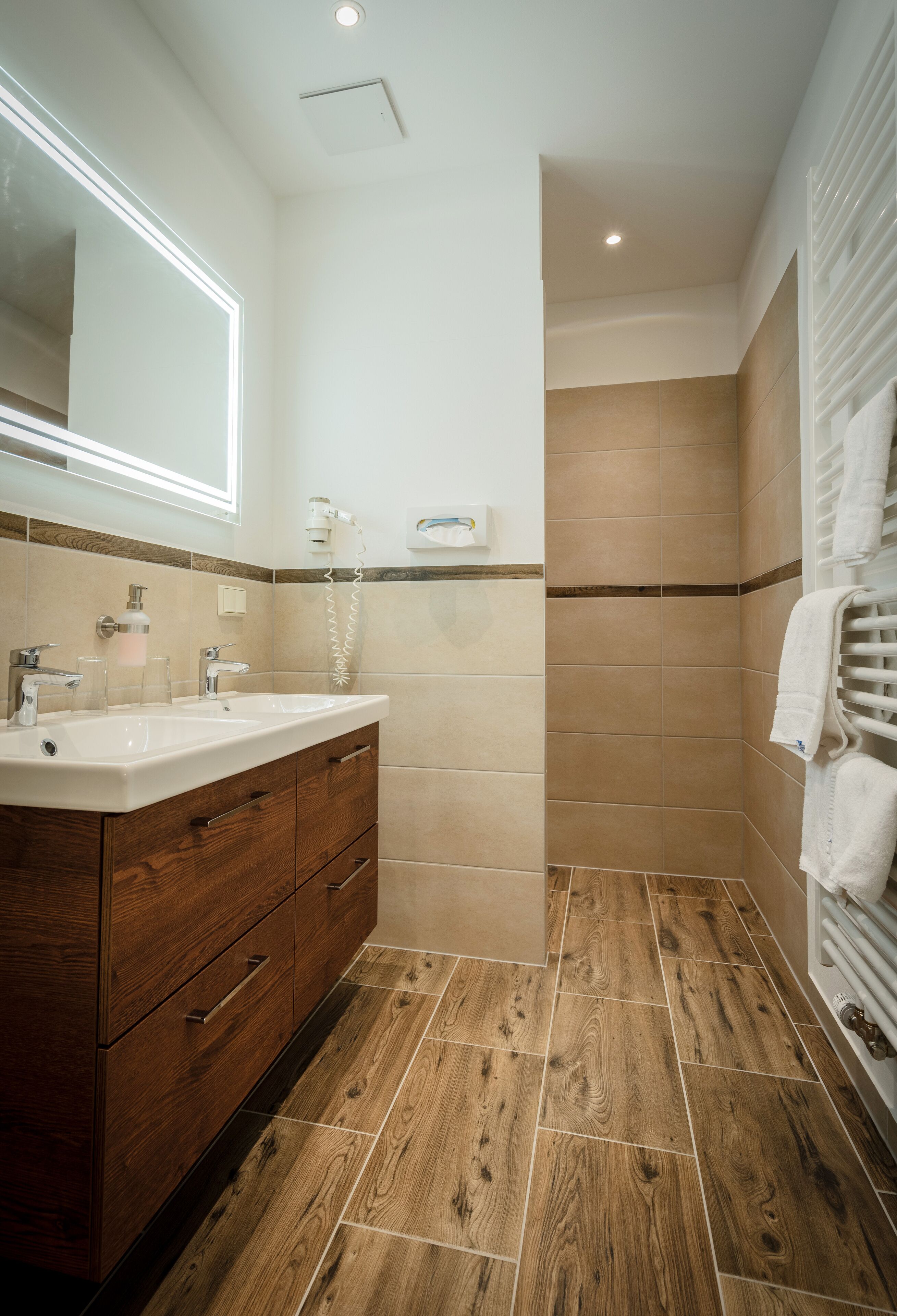 A bathroom with a wooden vanity, two sinks, a large mirror, and a shower area.