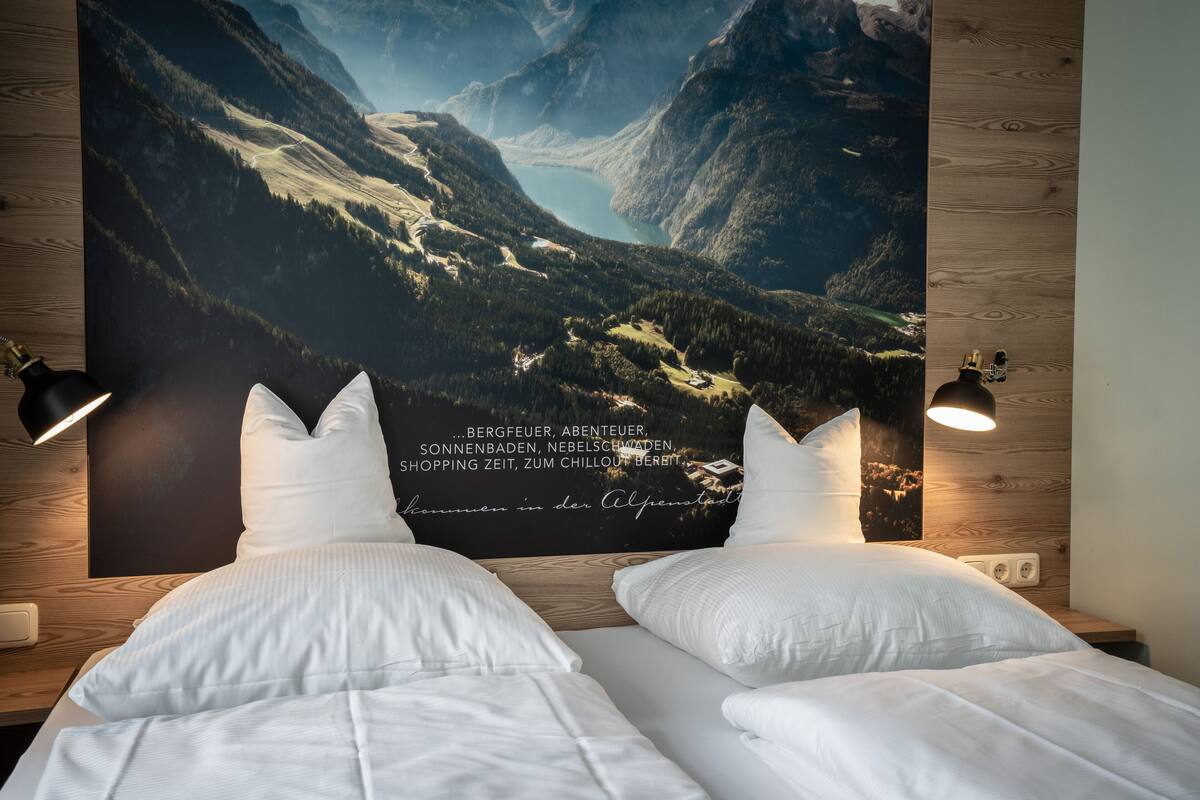 Un dormitorio con dos camas, un cartel grande con un paisaje de montaña en la pared y dos lámparas de noche.