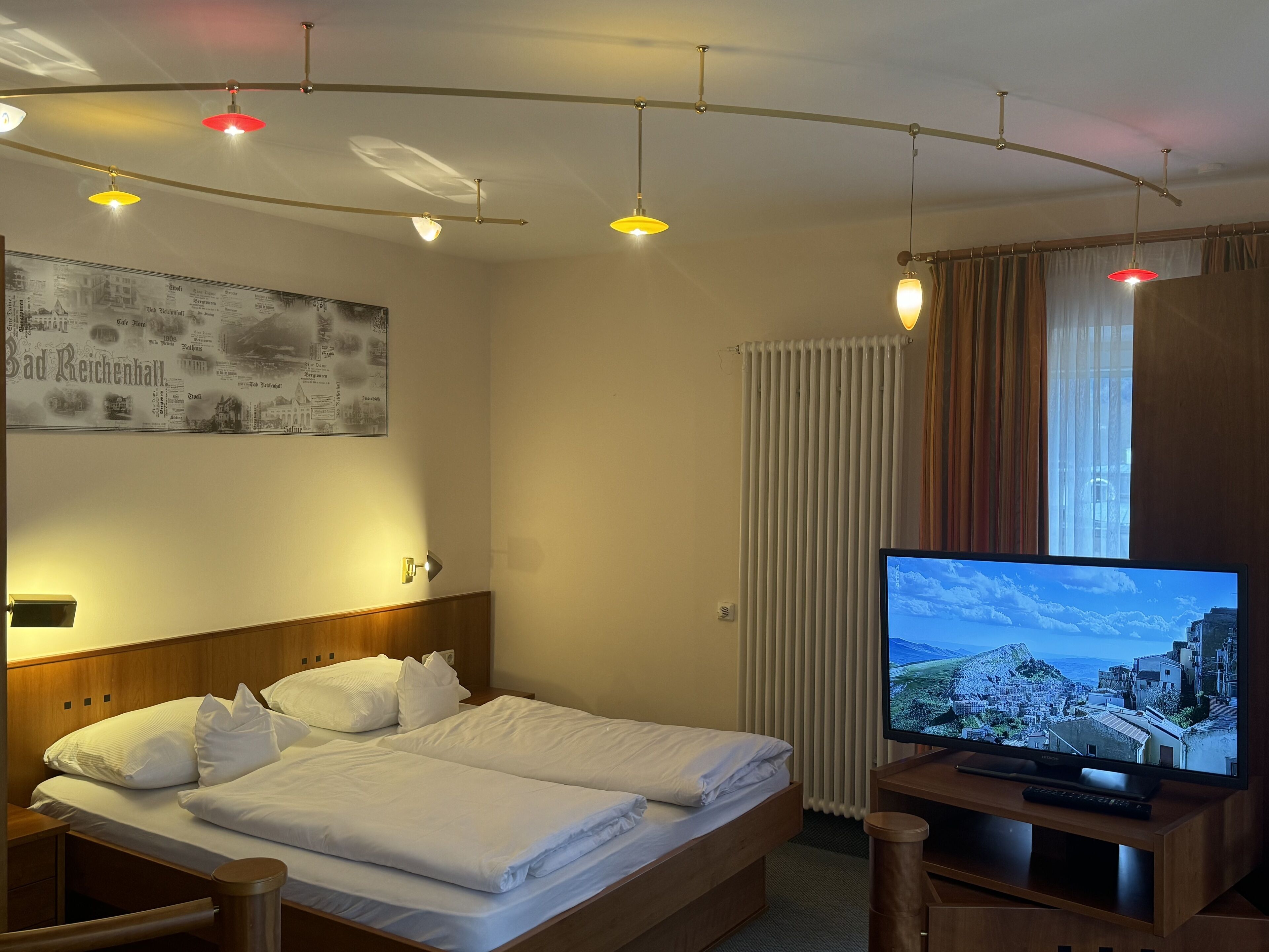Una habitación de hotel con cama, televisión y lámpara de pared.