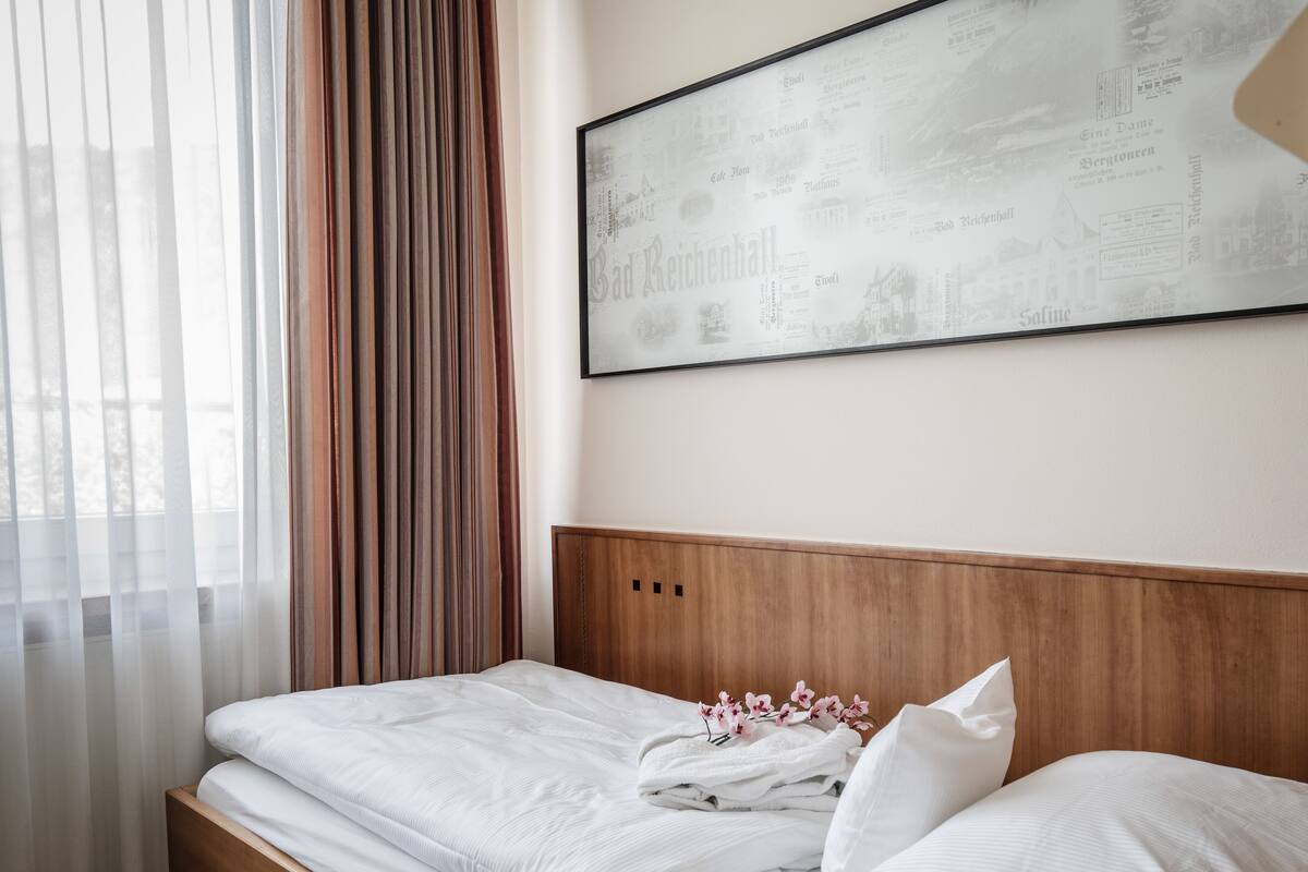 Una cama bien hecha con sábanas y almohadas blancas, un cabecero de madera y una obra de arte con una vista urbana enmarcada en la pared.