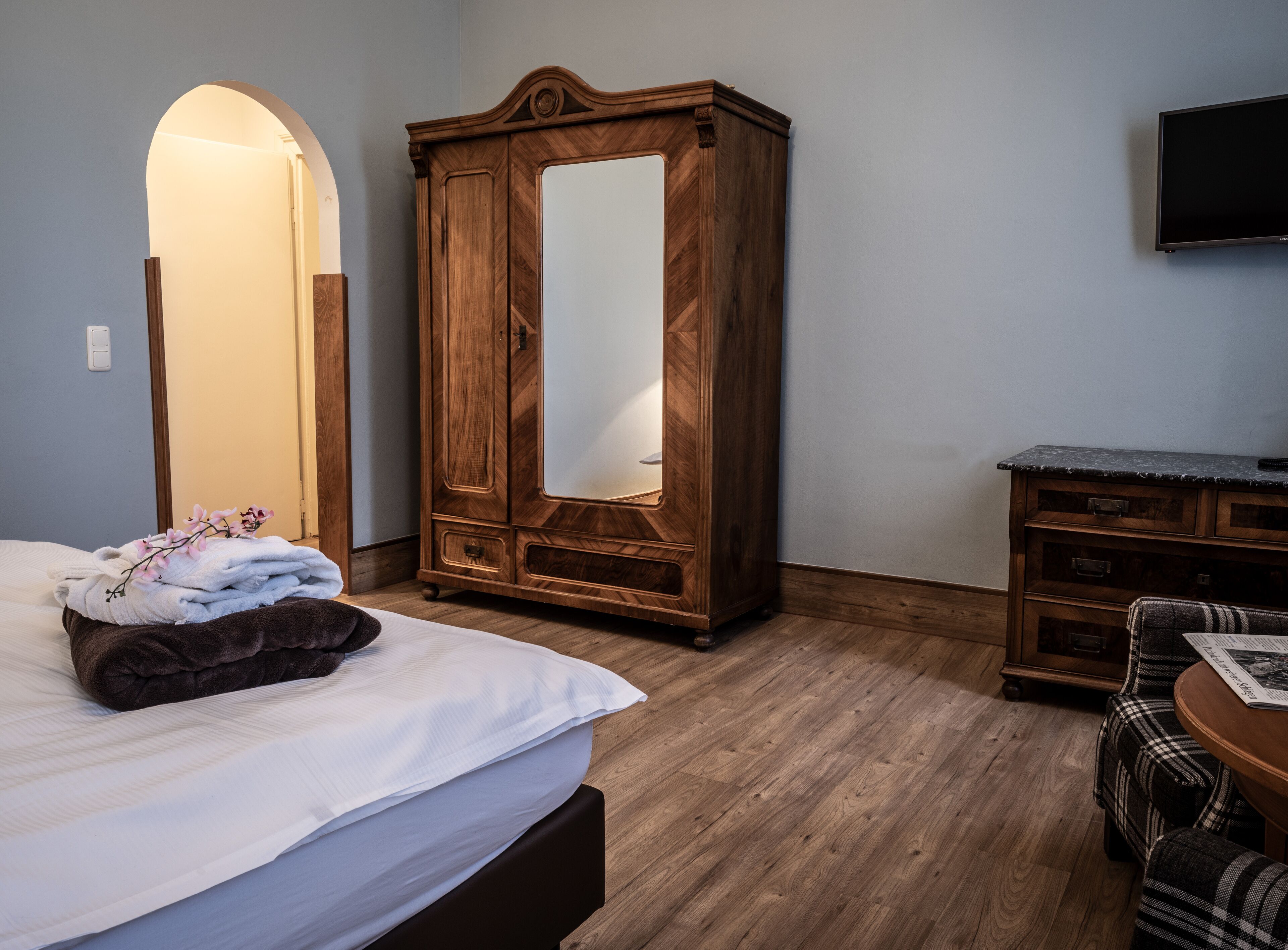 Un dormitorio con cama, un armario de madera con espejo, cómoda y televisor en la pared.
