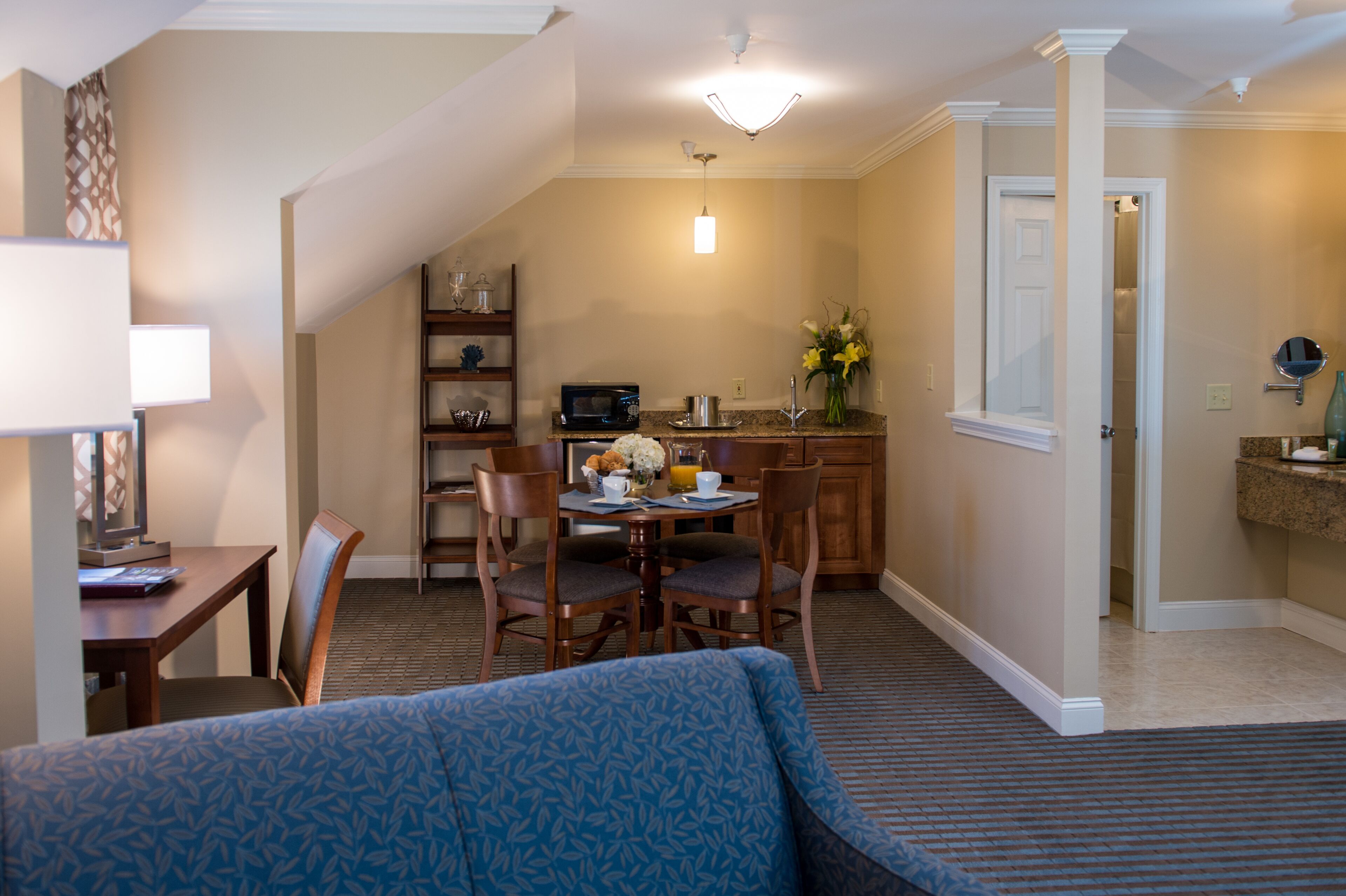 A compact hotel room with a dining area, a kitchenette, a sofa, and a small bathroom.