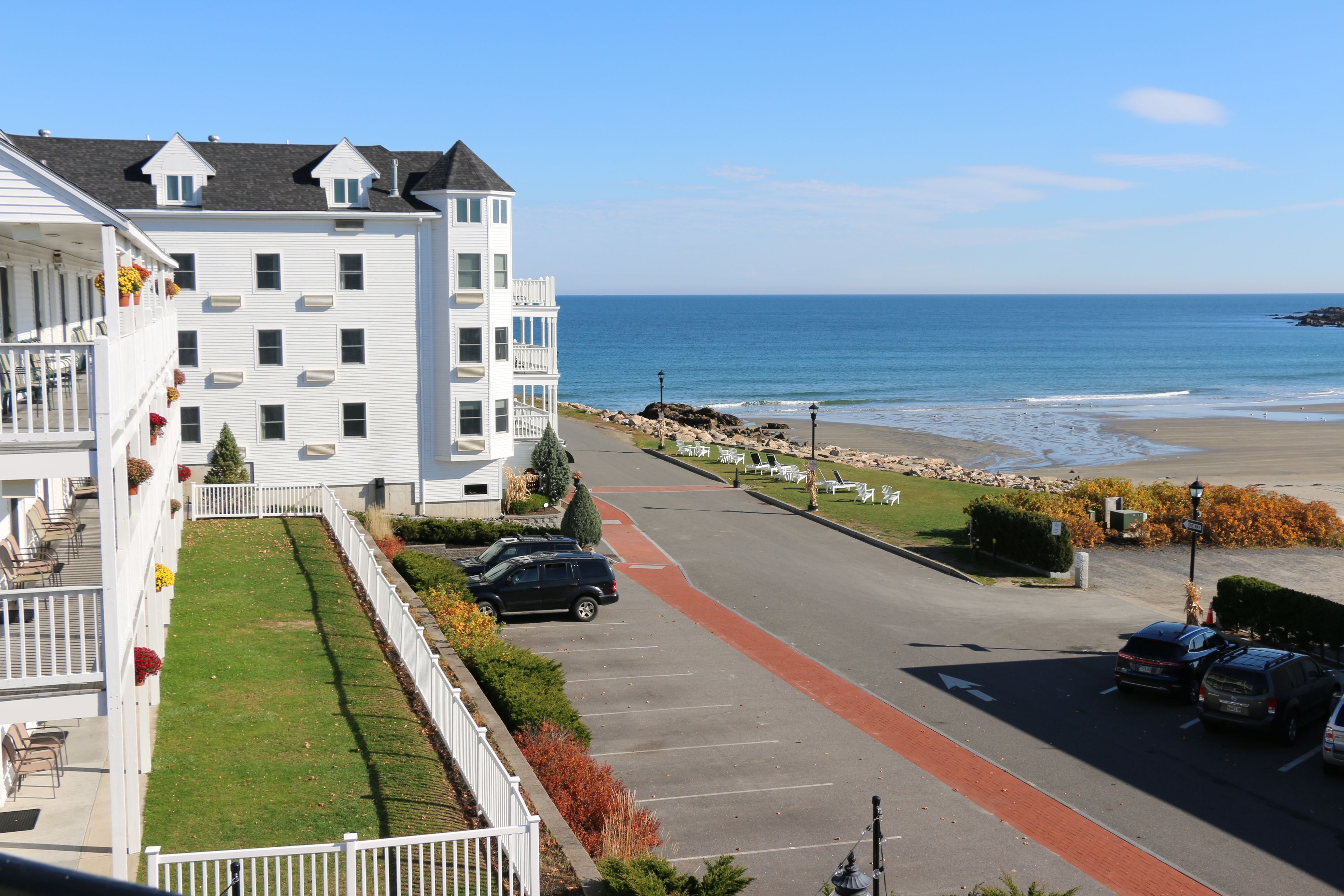 A multi-story white building with a balcony, a parking area, and a view of the beach.