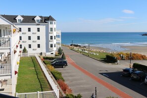A multi-story white building with a balcony, a parking area, and a view of the beach.