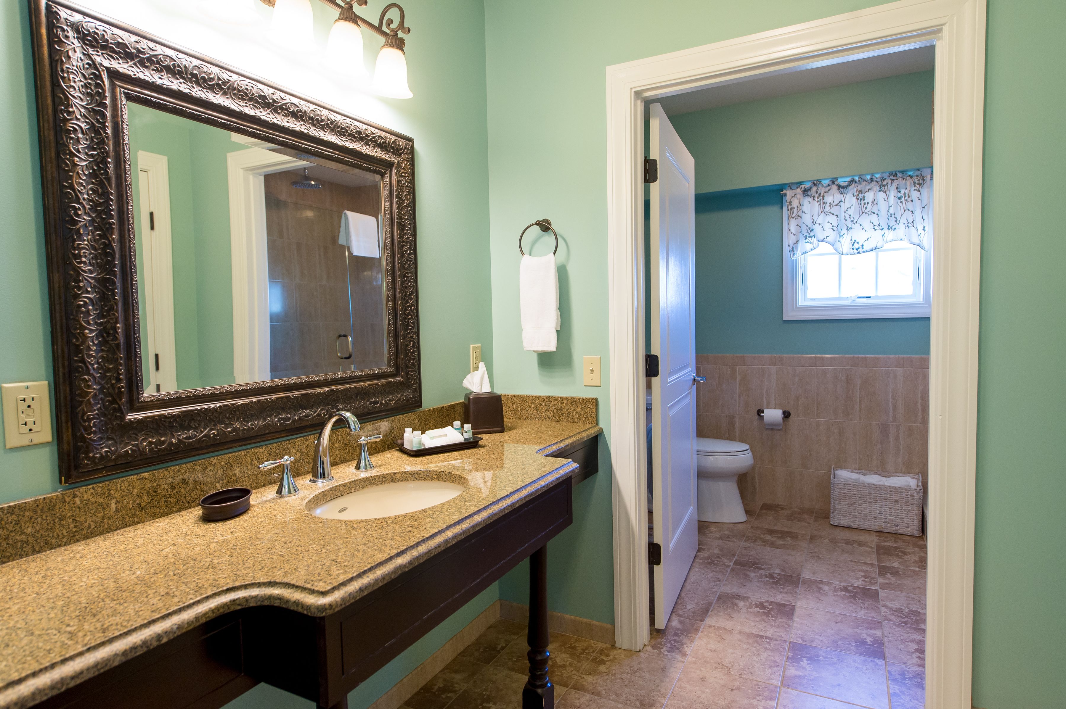 A bathroom with a granite countertop, a large mirror, a sink, and a toilet.