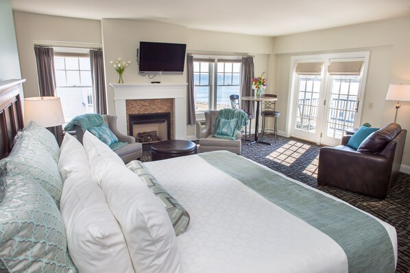 Quarto de hotel com uma cama grande, lareira, televisão e varanda com vista para o mar.