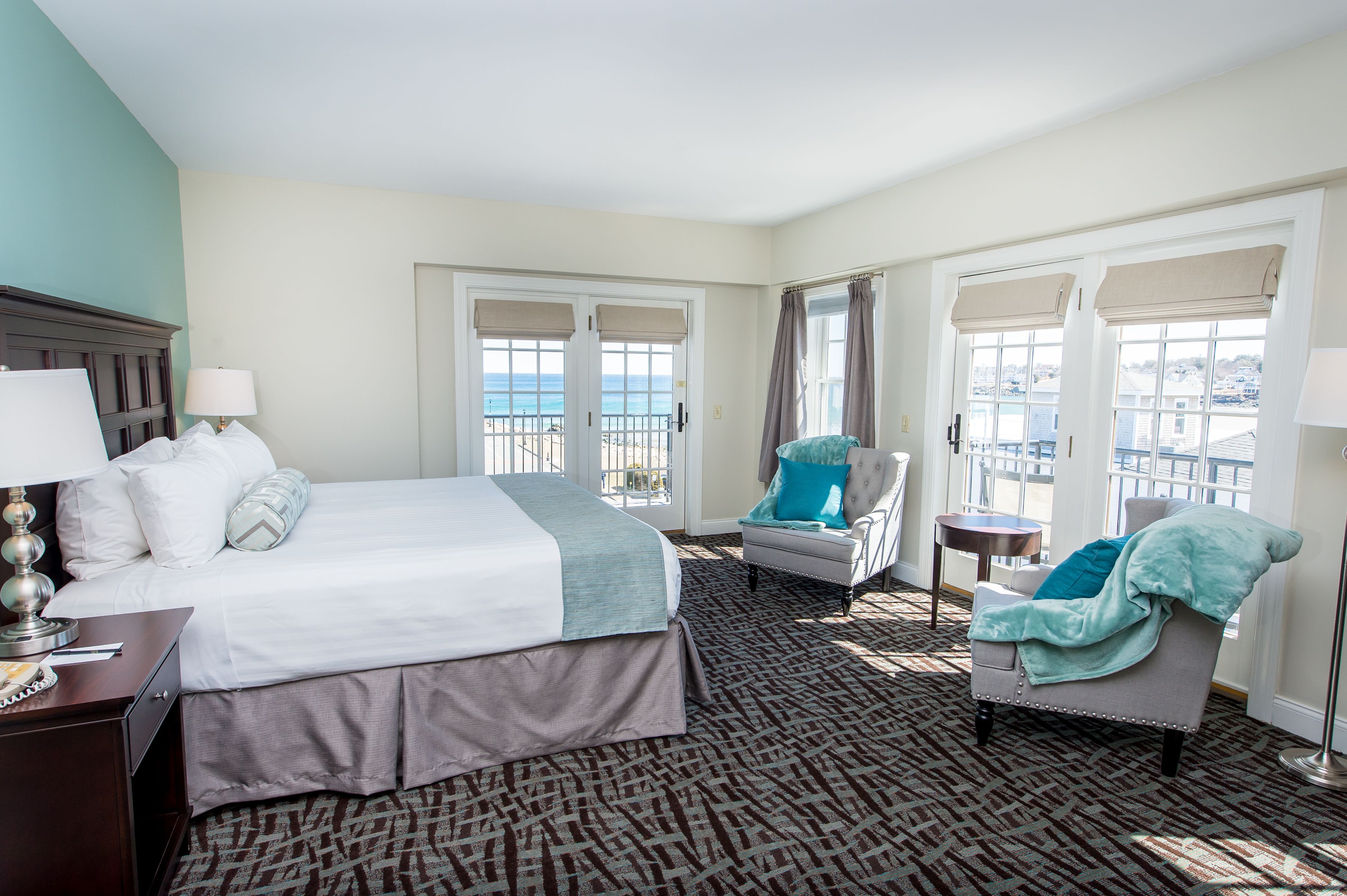 Une chambre d’hôtel avec un lit, une chaise, une petite table et une vue sur la mer grâce à de grandes fenêtres.