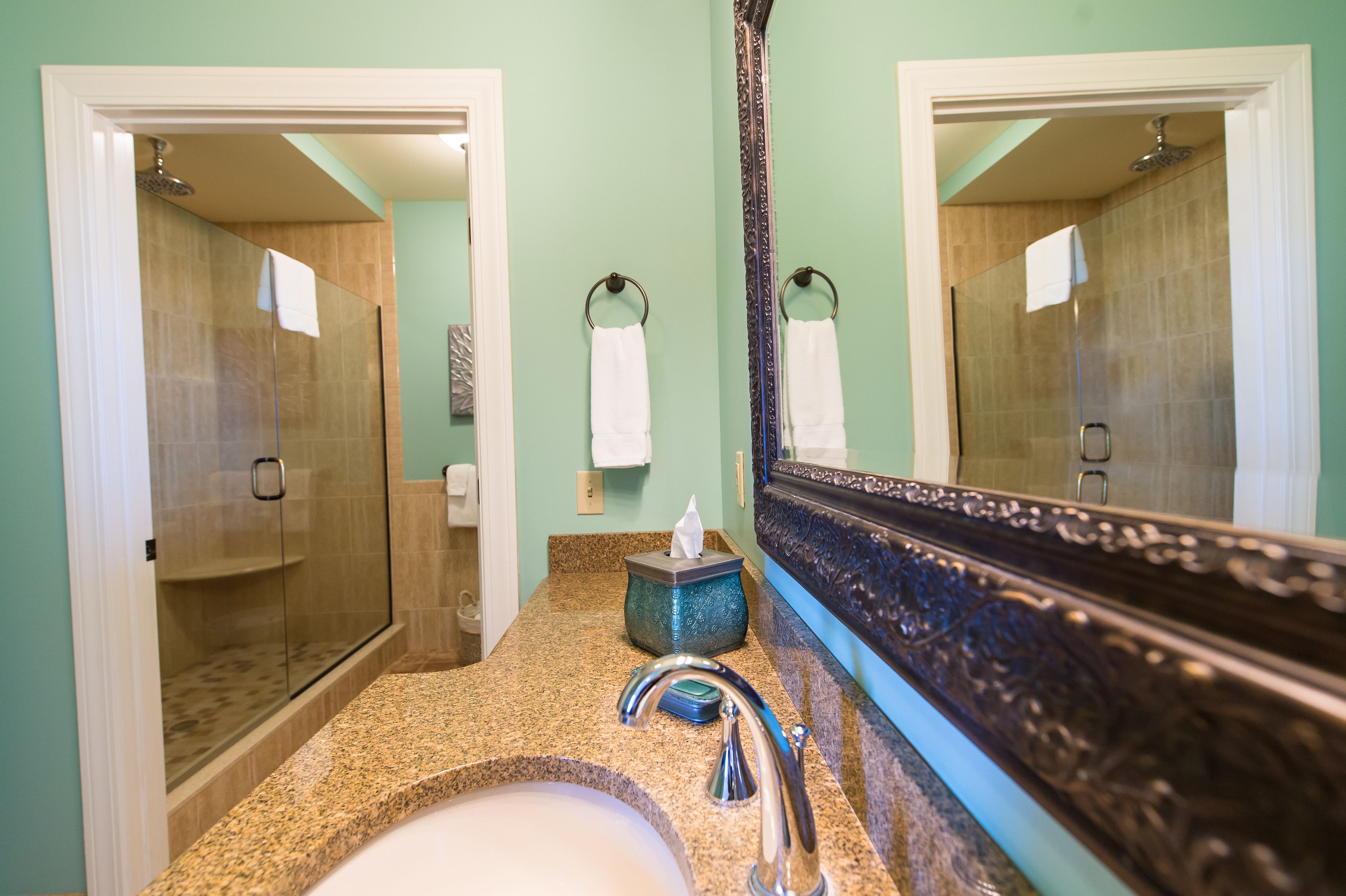 A bathroom with a granite countertop, a sink, a mirror, and a glass-enclosed shower.