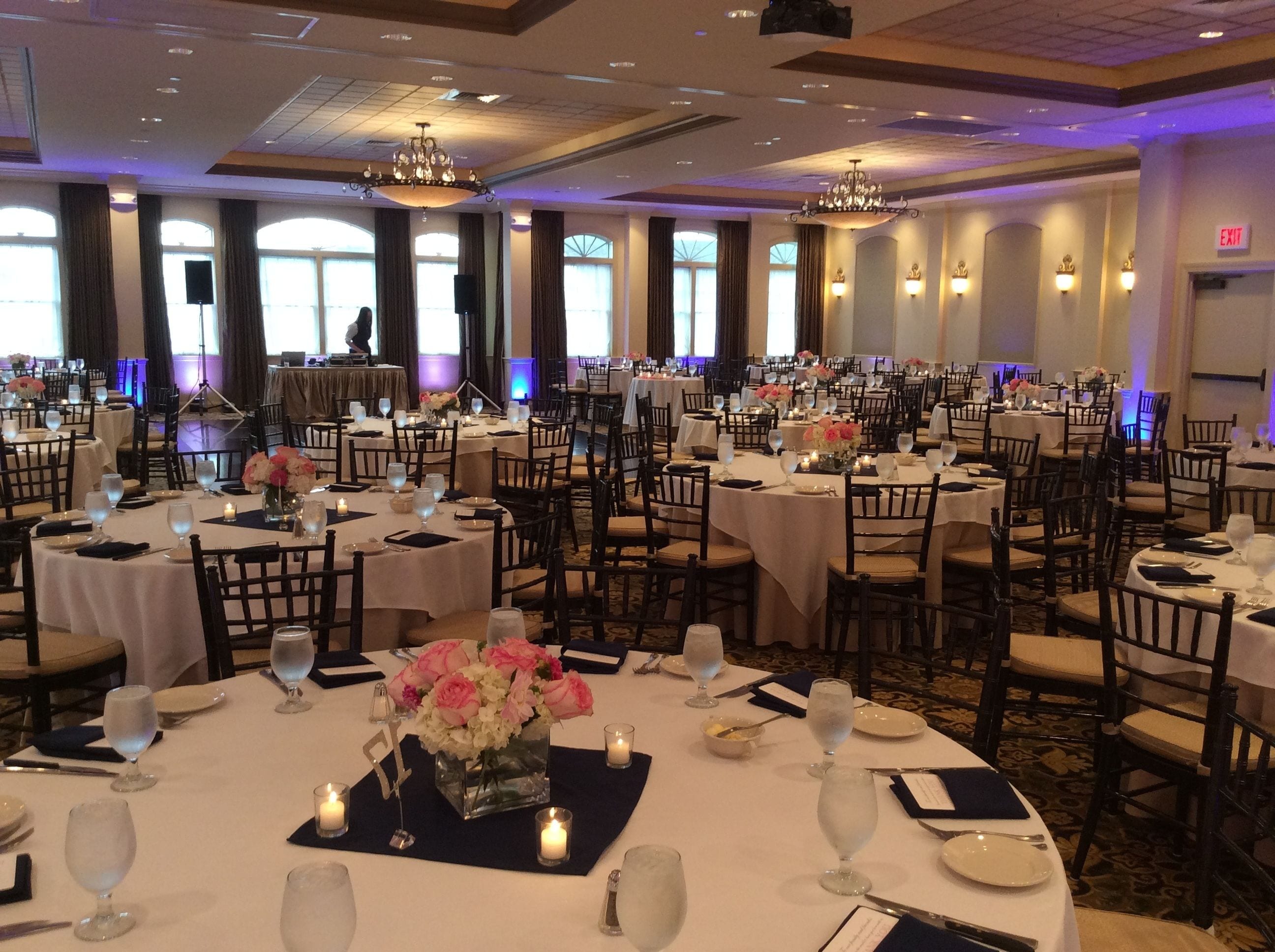 A banquet hall with round tables set for dining, featuring white tablecloths, chairs, and floral centerpieces.