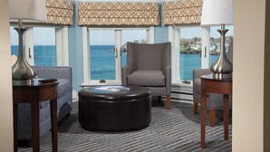 A corner room with a view of the sea, a grey armchair, a patterned sofa, and a round ottoman. - Union Bluff Hotel & Meeting House (York Beach)