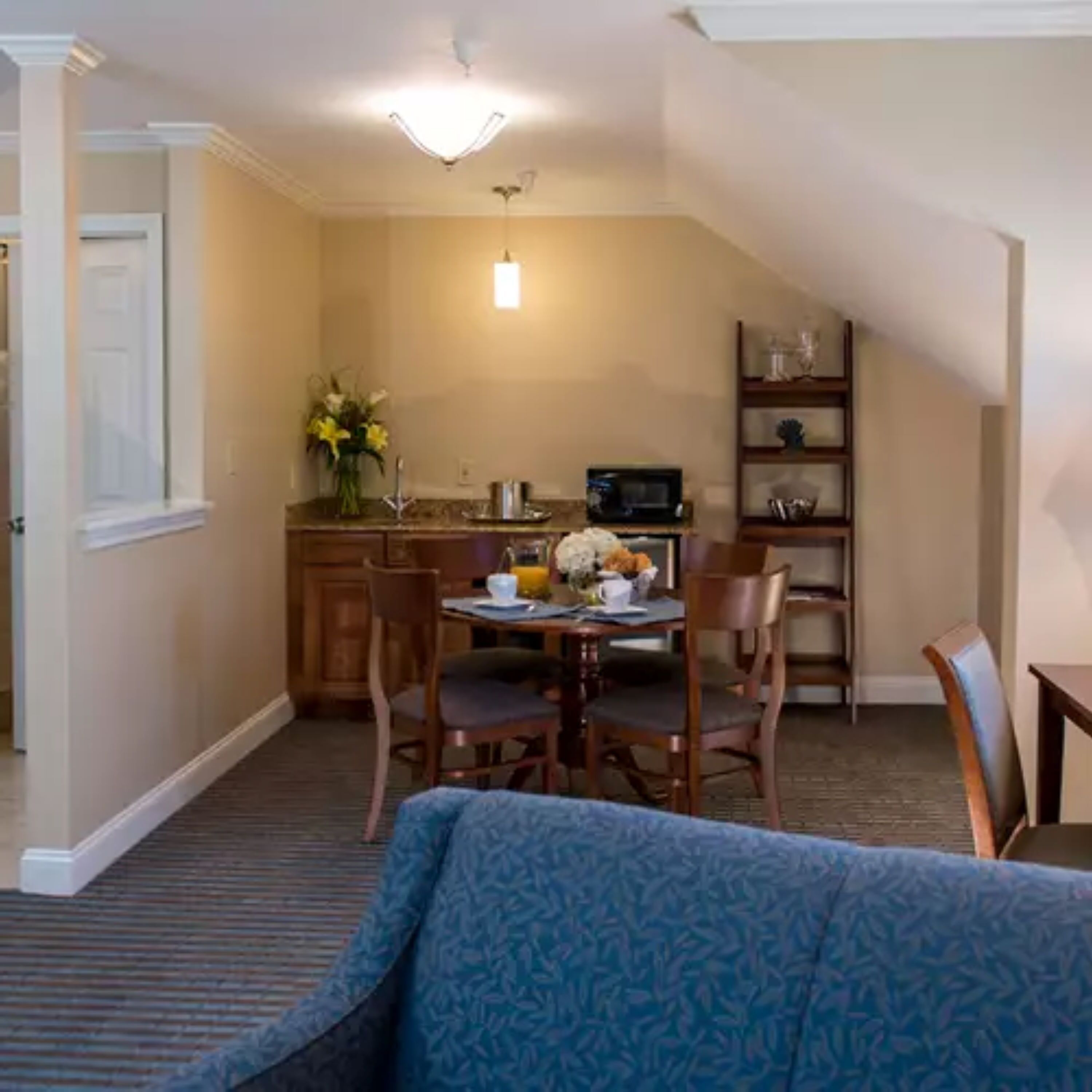 A dining area with a table set for two, chairs, a microwave, and a shelf with decorative items.