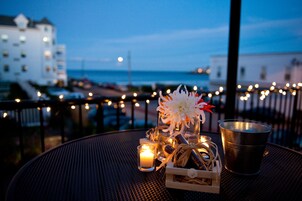Uma mesa com uma vela, um arranjo de flores e uma xícara de metal, com vista para um edifício e um corpo d'água.