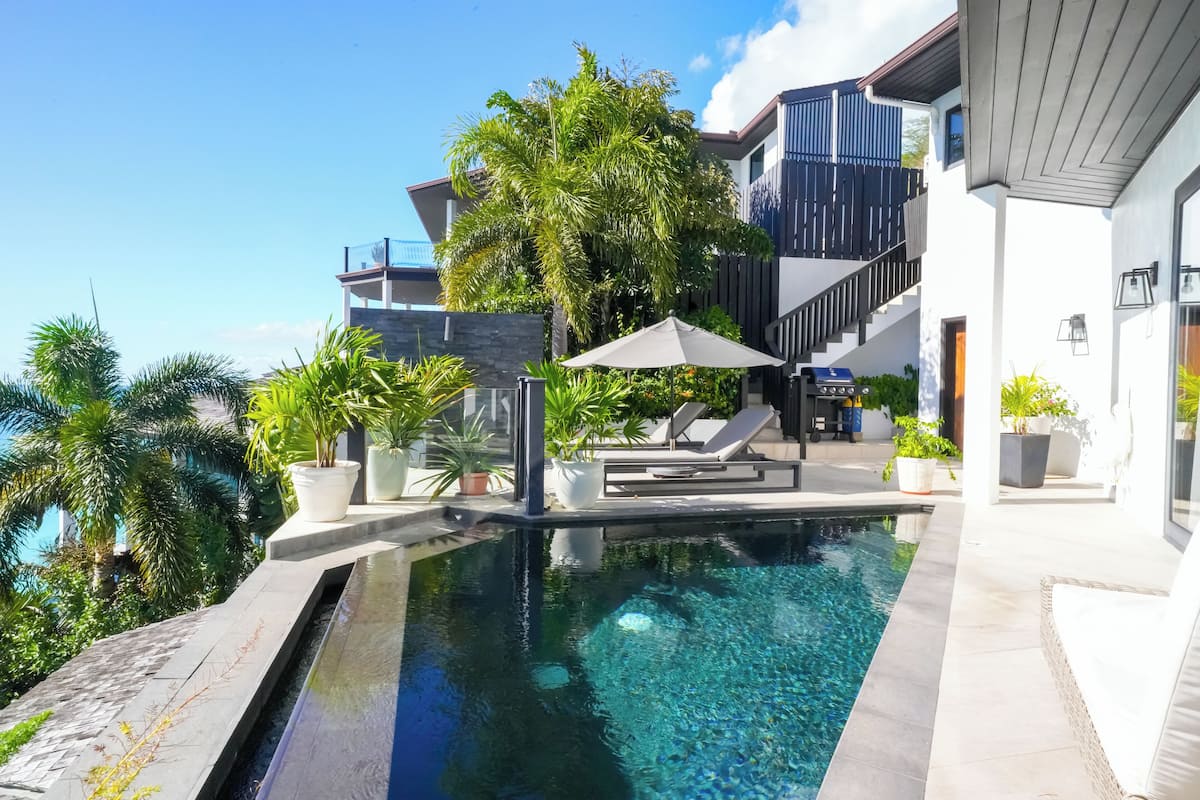 A modern pool area with a clear pool, lounge chairs, and potted plants.