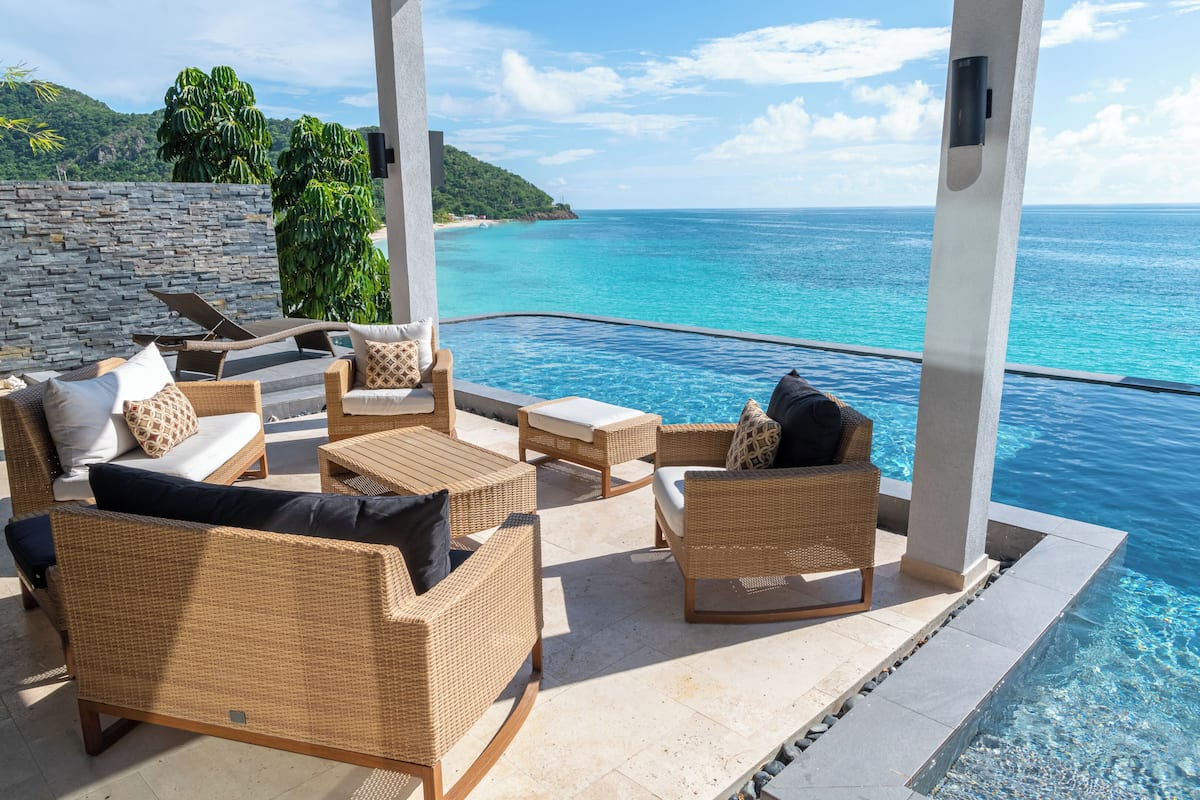 A poolside area with wicker furniture and a view of the ocean.