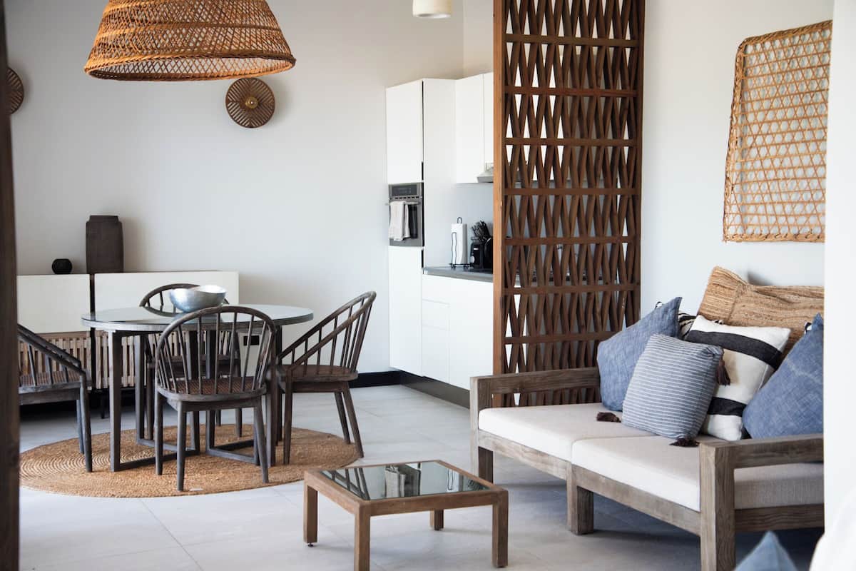A modern kitchen with white cabinets, a dining area with a round table and chairs, and a living area with a sofa and cushions.