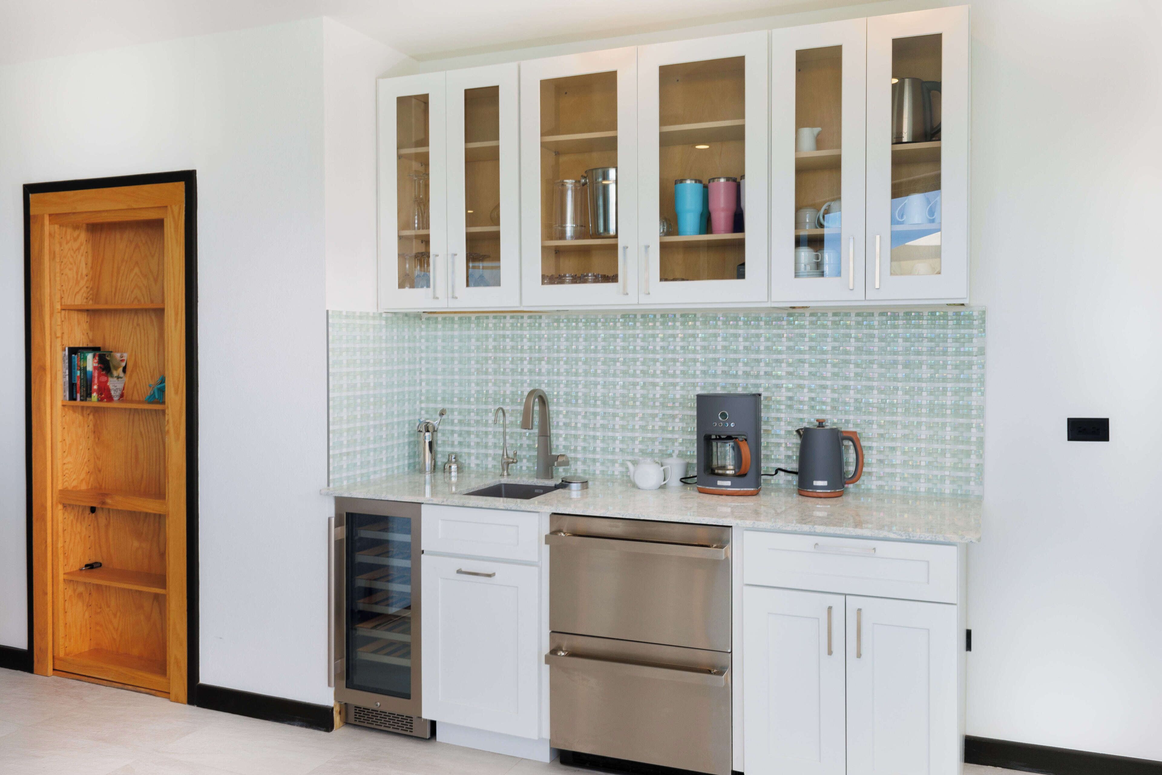 Una cocina con armarios blancos, lavavajillas, cafetera y salpicadero de azulejos.