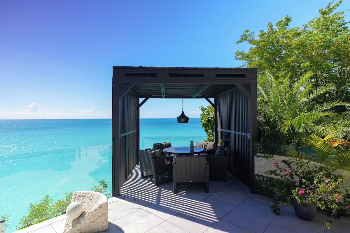 A covered outdoor seating area with a view of the ocean, a hanging light fixture, and potted plants.