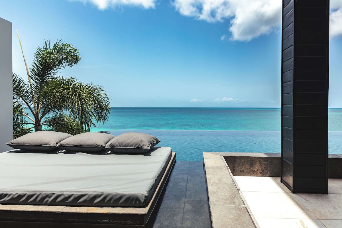 A bedroom with a view of the ocean, a bed with pillows, and a small pool.