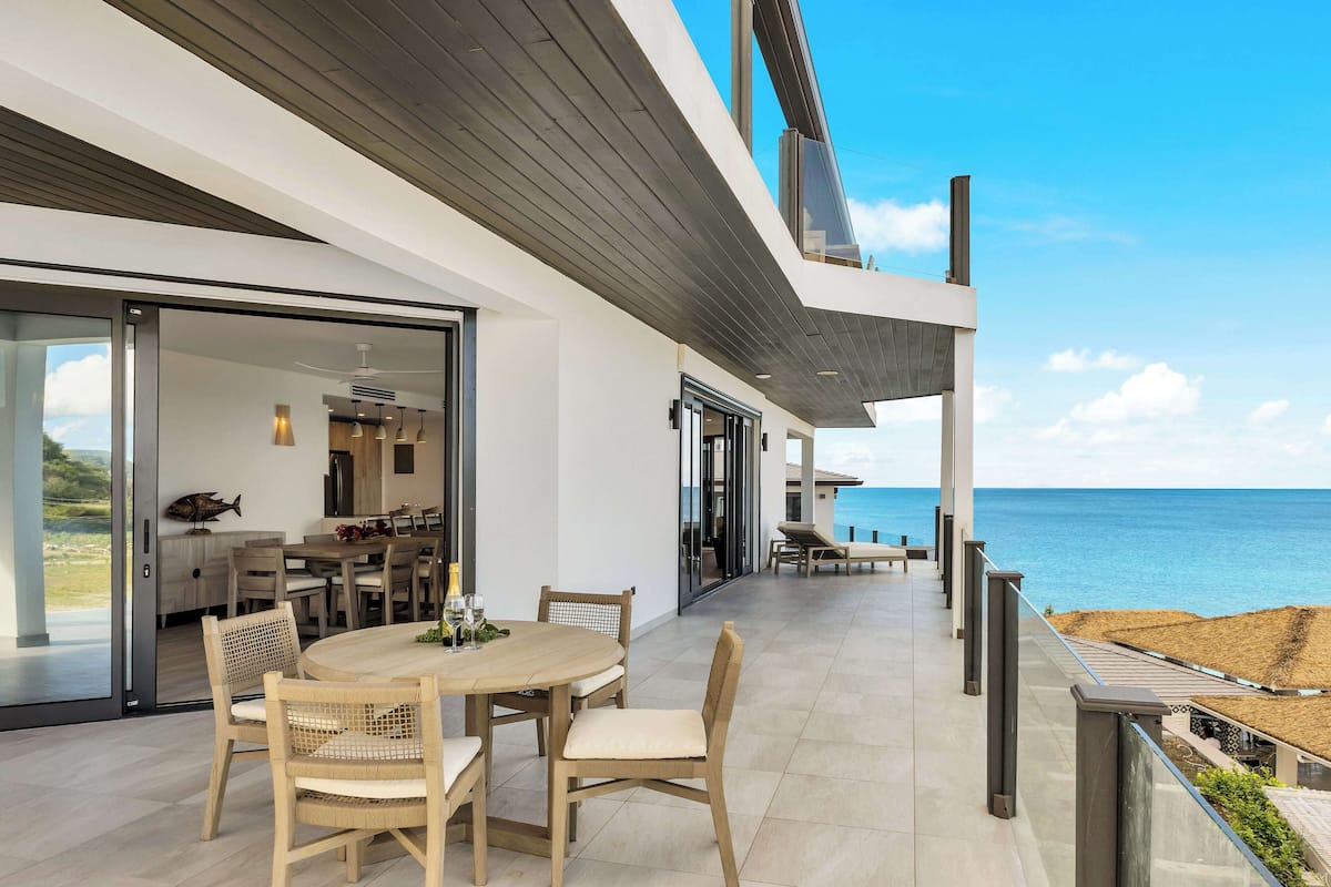A modern outdoor dining area with a view of the sea, featuring a round table and wicker chairs.