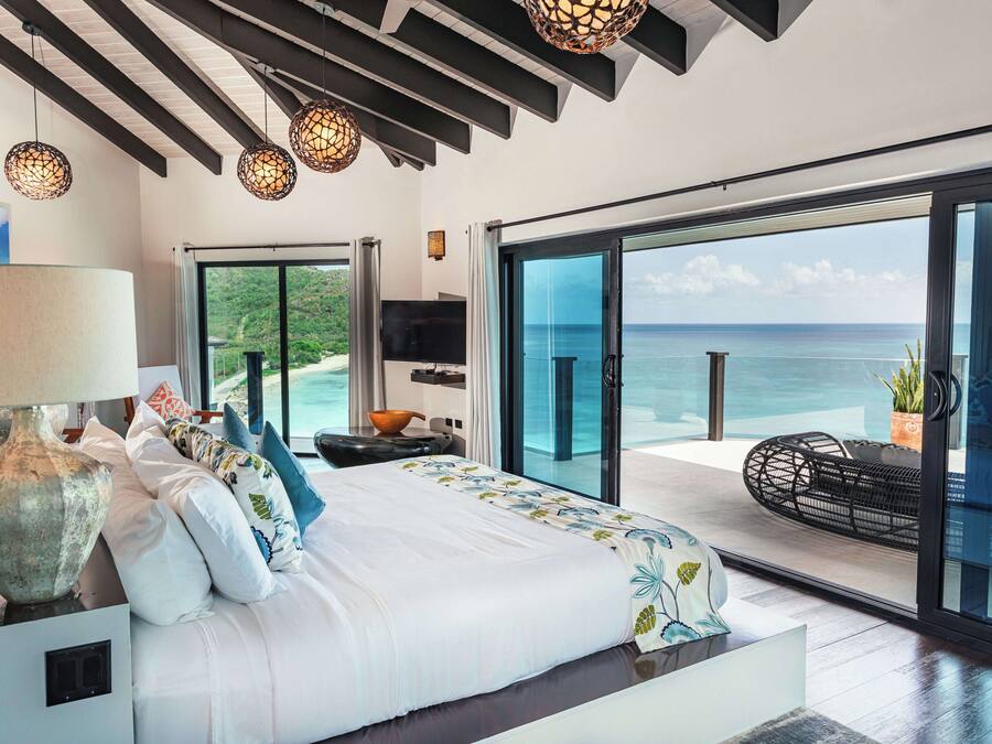 A bedroom with a large bed, a TV, and a view of the ocean.