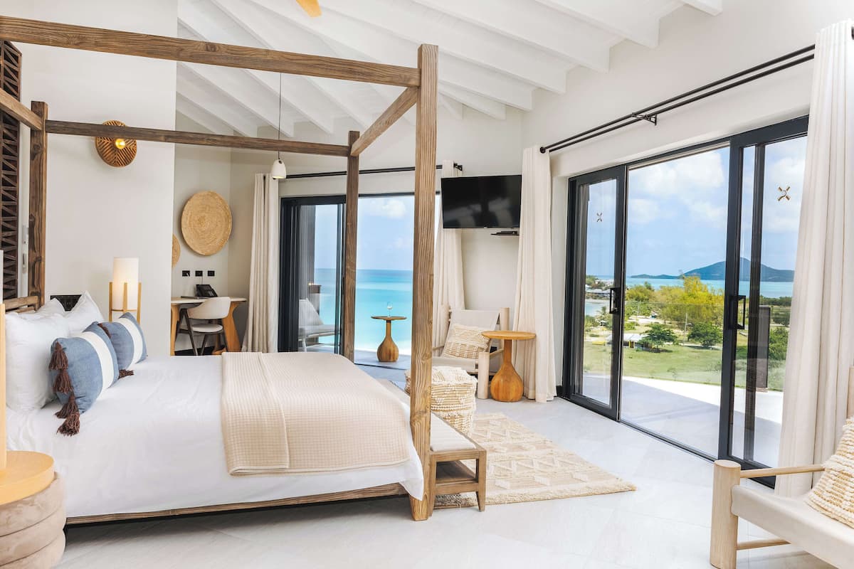 A spacious bedroom with a large bed, a TV, and a balcony with a view of the sea.