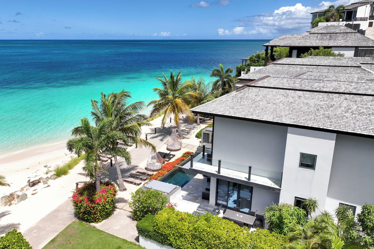 A beachfront property with a pool, palm trees, and a view of the ocean.