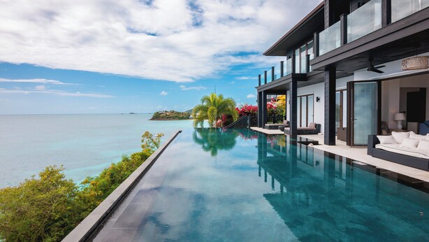 Piscina infinita moderna com vista desimpedida para o oceano, varanda com área de estar externa e jardim tropical.