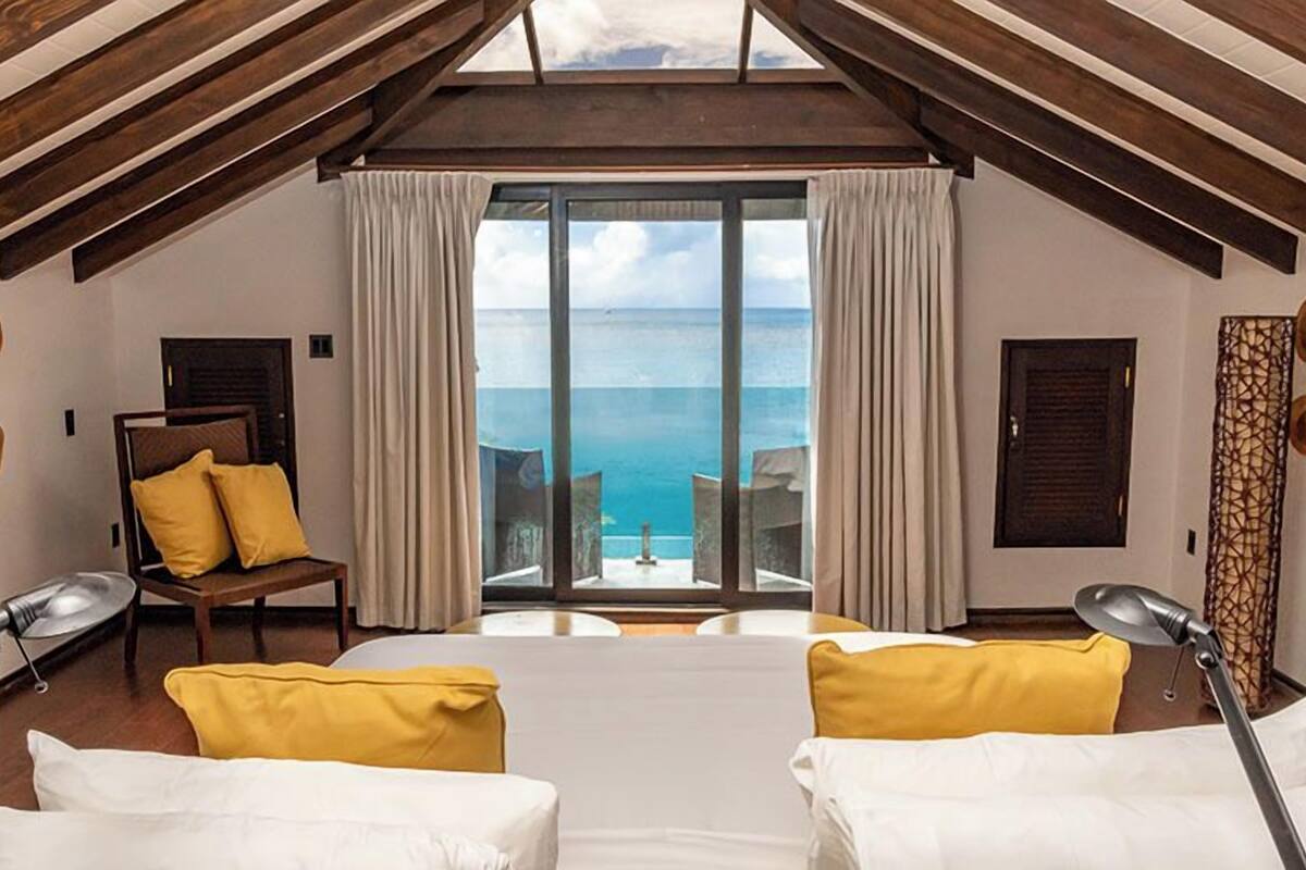 A room with a bed, two chairs, a table, and a view of the sea.