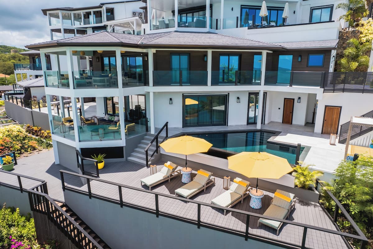 A modern multi-story house with a rooftop pool area featuring sun loungers and umbrellas.