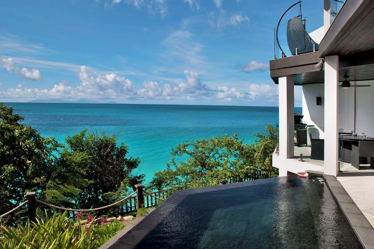 A modern infinity pool overlooking a turquoise sea with a clear sky.