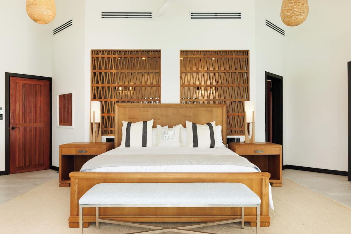 A bedroom with a wooden bed, two bedside tables, a bench, a wooden partition, and a door.