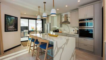 A modern kitchen with a central island, pendant lighting, stainless steel appliances, and a view to the outside.