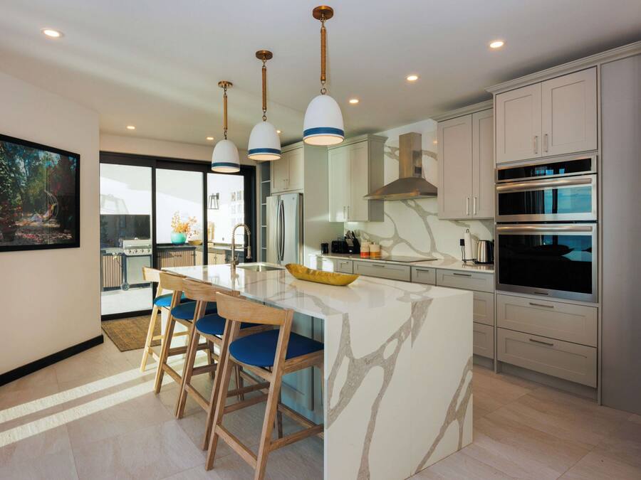 A modern kitchen with a central island, pendant lighting, stainless steel appliances, and a view to the outside.