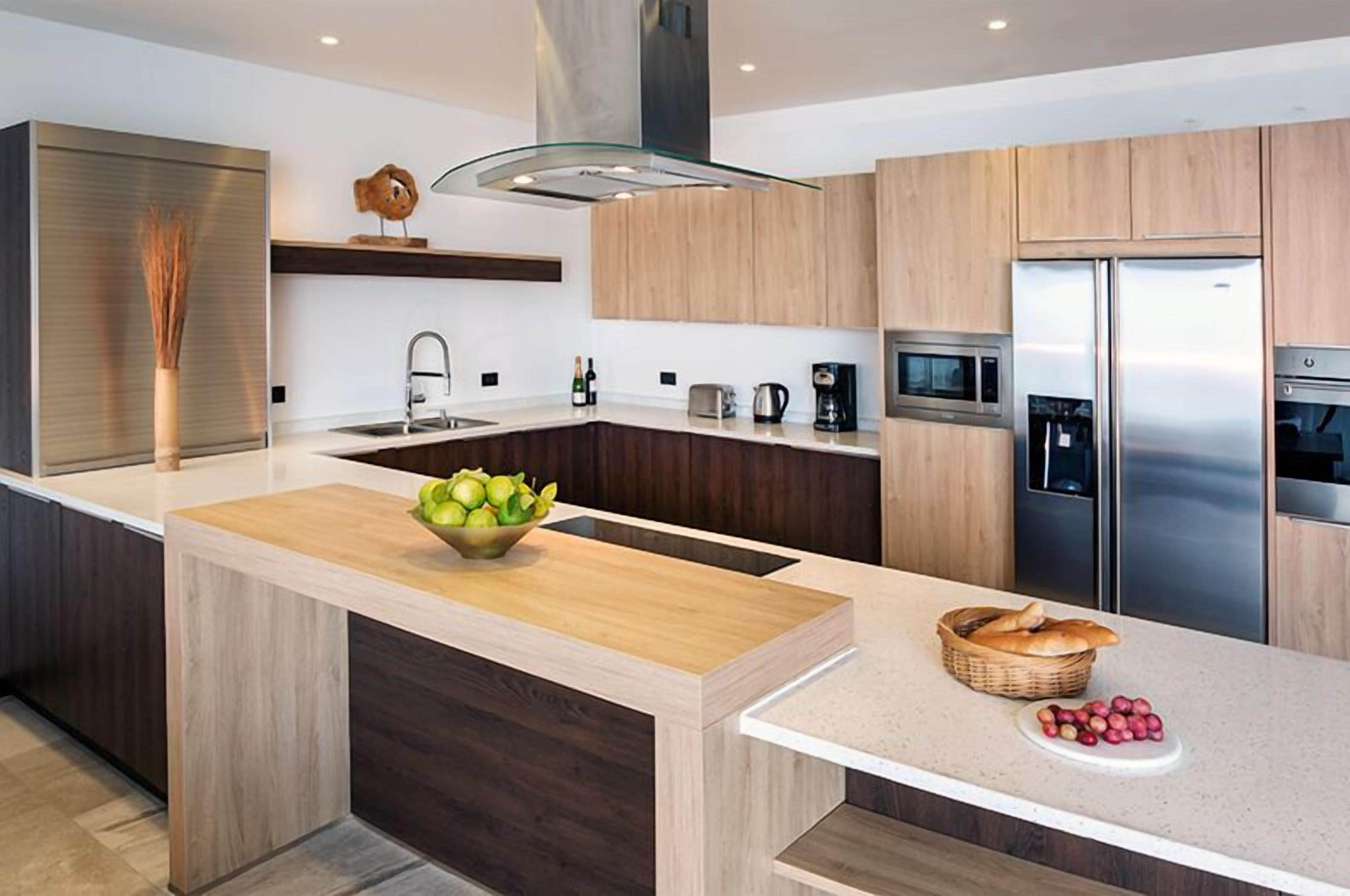 A modern kitchen with a central island, wooden cabinets, stainless steel appliances, and a glass pendant light.