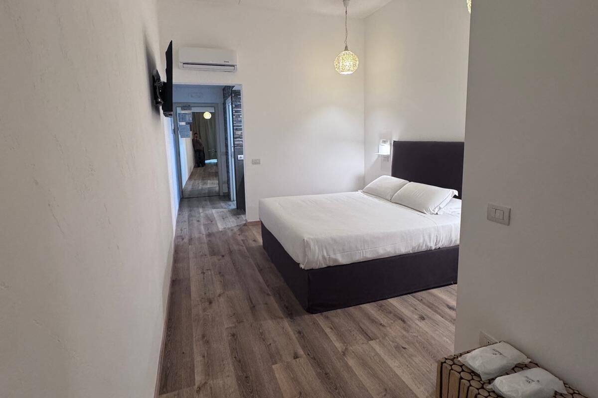 Ein modernes Schlafzimmer mit Holzboden, einem Bett mit weißer Bettwäsche, einer hängenden Leuchte und einem kleinen Holzschemel.