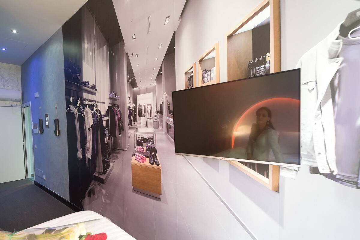 Ein moderner Hotelkorridor mit Kleiderstangen, Schuhpräsentation und einem Fernsehbildschirm.