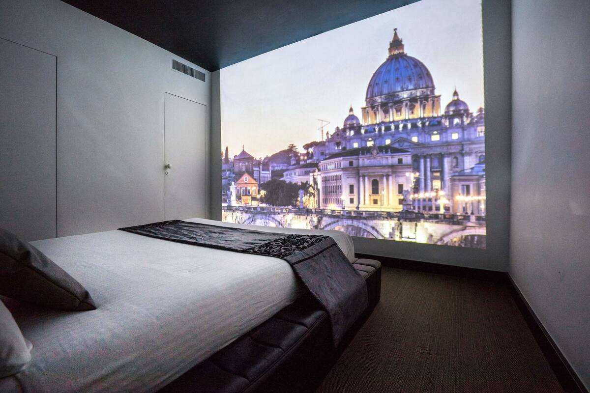 Ein Hotelzimmer mit einem Bett, einem großen Fenster und einer Projektion einer Stadtansicht.