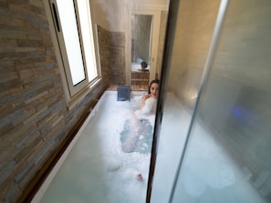 A spa room with a stone wall, a bathtub with bubbles, and a wooden door in the background.