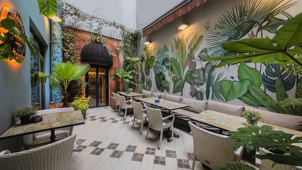 An outdoor patio with wicker furniture, a mural of tropical plants, and a brick wall. - Ayramin Deluxe Hotel  (Istanbul)