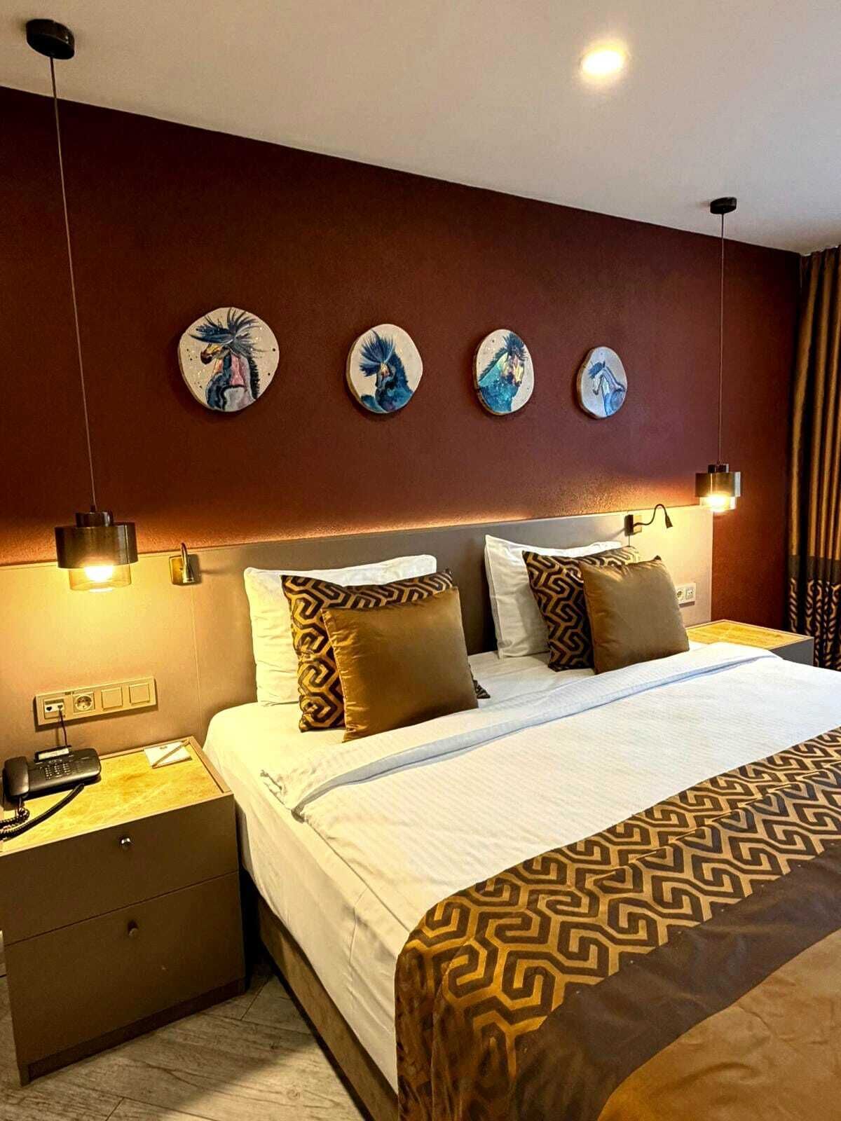 Una habitación de hotel con cama, mesitas de noche, teléfono y decoración en la pared.