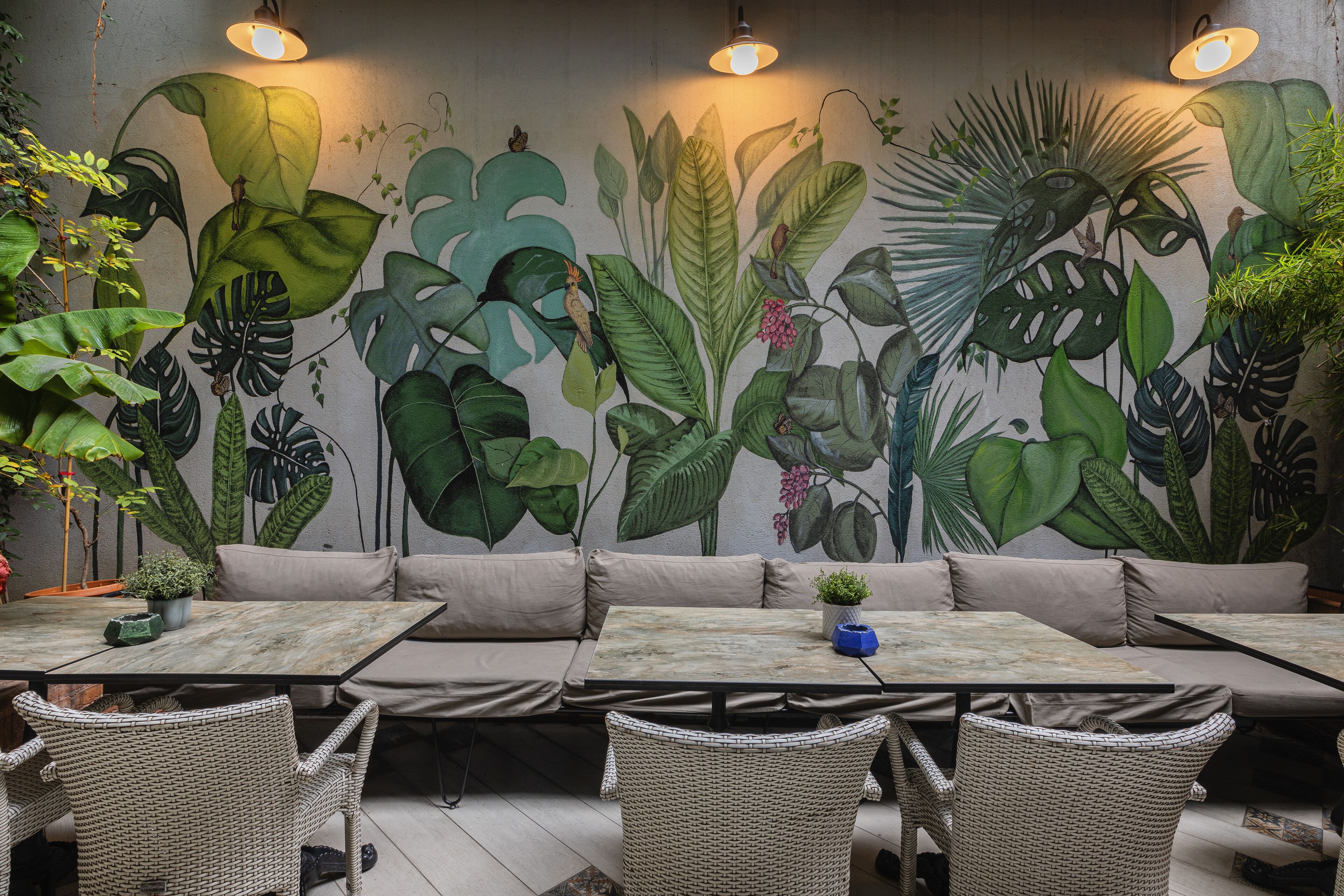 A restaurant with a mural of tropical plants, wicker furniture, and tables with blue centerpieces.
