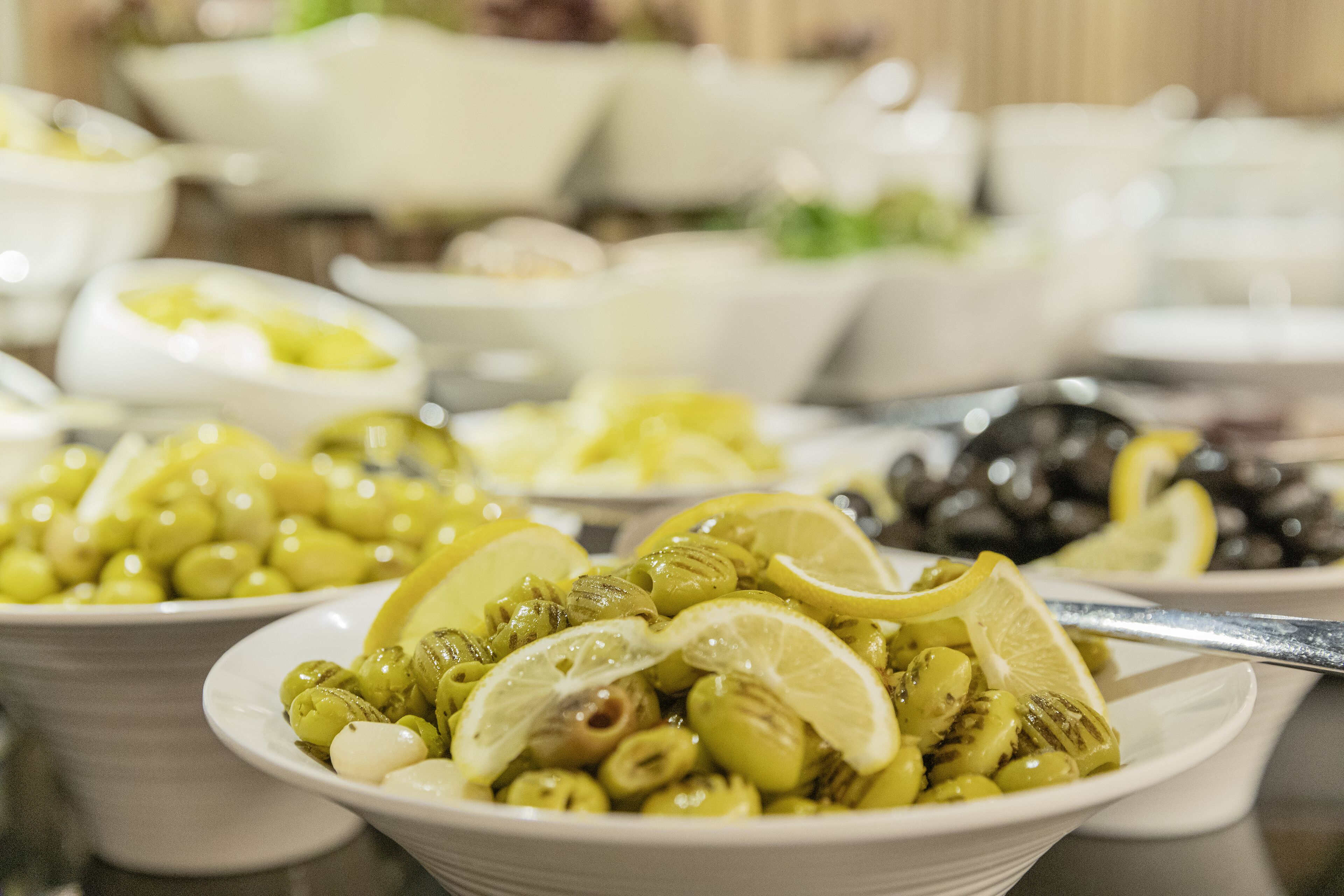 A buffet with various dishes, including olives and lemon slices.