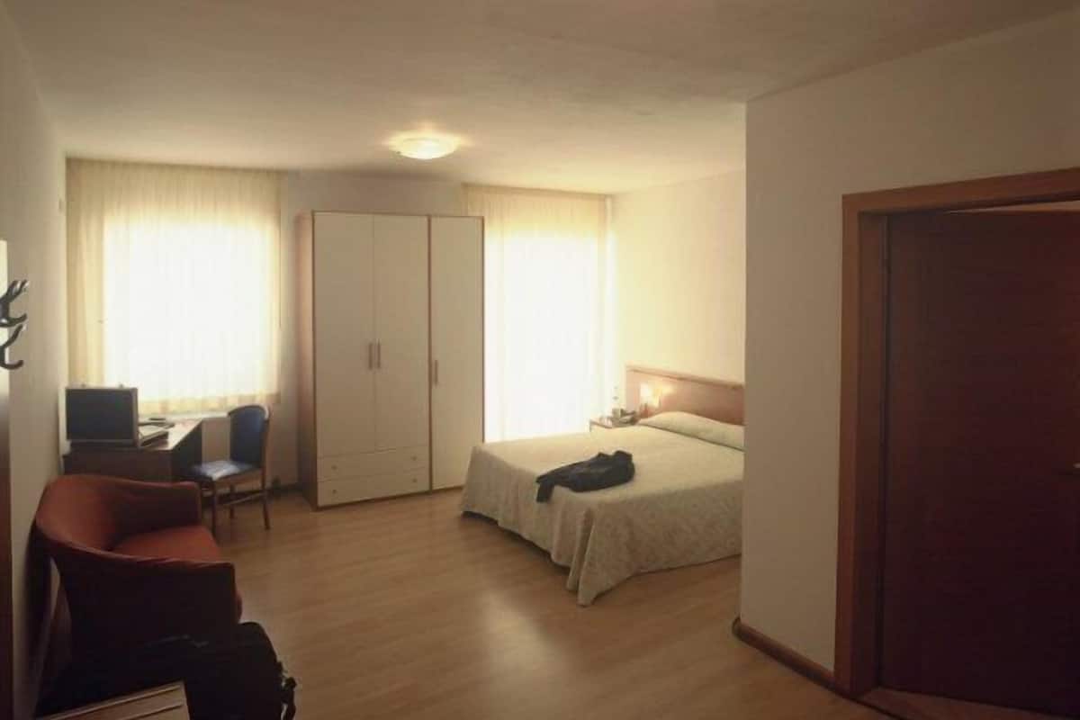 Ein Hotelzimmer mit Bett, Schreibtisch mit Stuhl, Kleiderschrank und einer Tür.