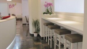 A modern reception area with a curved counter, a white wall with a large window, and a row of bar stools. - Hotel Ristorante Scaranò (Levico Terme)