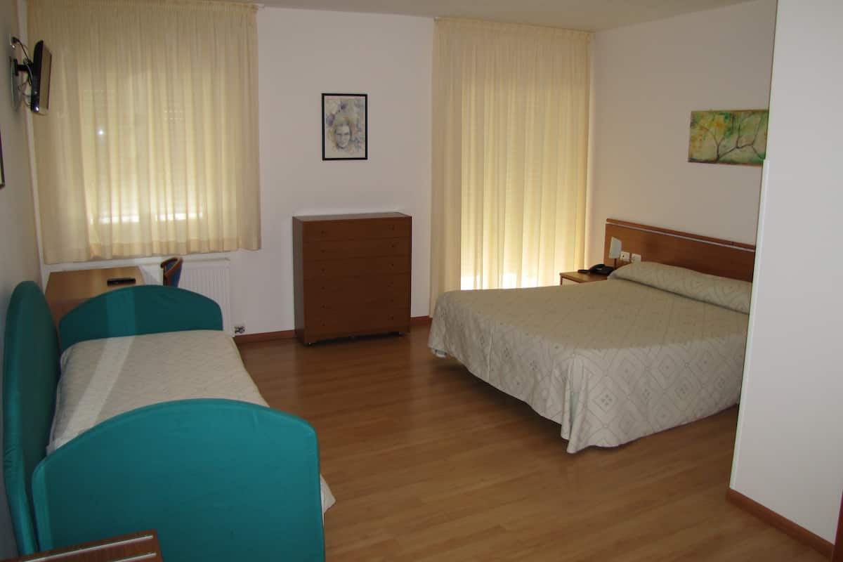 Ein Hotelzimmer mit zwei Betten, einer Holzkommode, einem Schreibtisch mit Stuhl und einem Bild an der Wand.